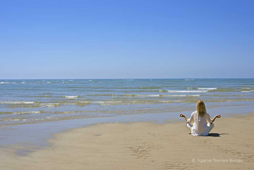 Woman meditating ion Algarve beach